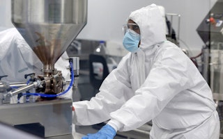 A production scientist works with samples at Afrigen Biologics in Cape Town, South Africa, on February 3, 2022. Photo credit: © Shelley Christians/Reuters A scientist wearing protective gear in a lab